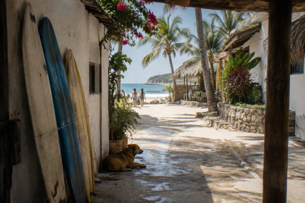A sandy beach town street lined with low buildings and surfboards resting against a wall