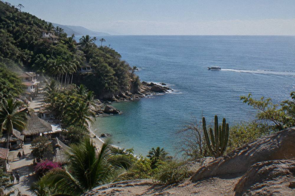 Small whale-watching boat moving across open water with Banderas Bay shoreline in the distance